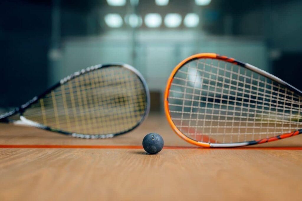 Two squash rackets on their edges and a squash ball lying on the floor of a squash court.