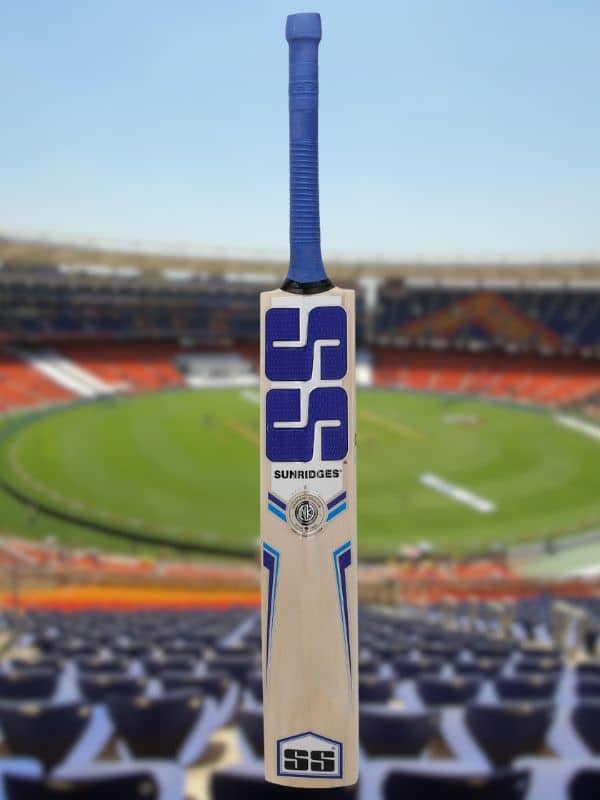 An SS cricket bat is centered in the frame, set against a softly blurred cricket stadium.
