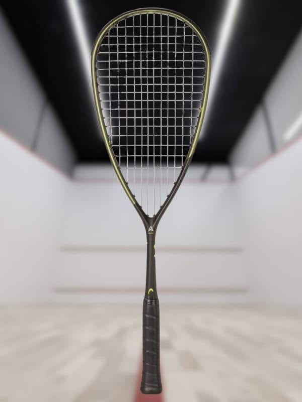 A squash tennis racket is centered in the frame, set against a softly blurred squash court.