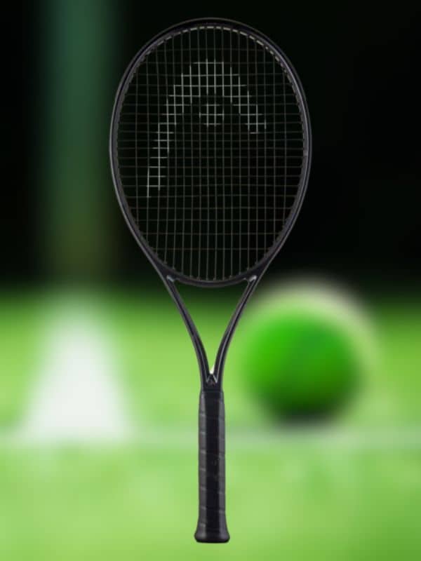 A black head tennis racket is centered in the frame, set against a softly blurred green tennis ball and court background.